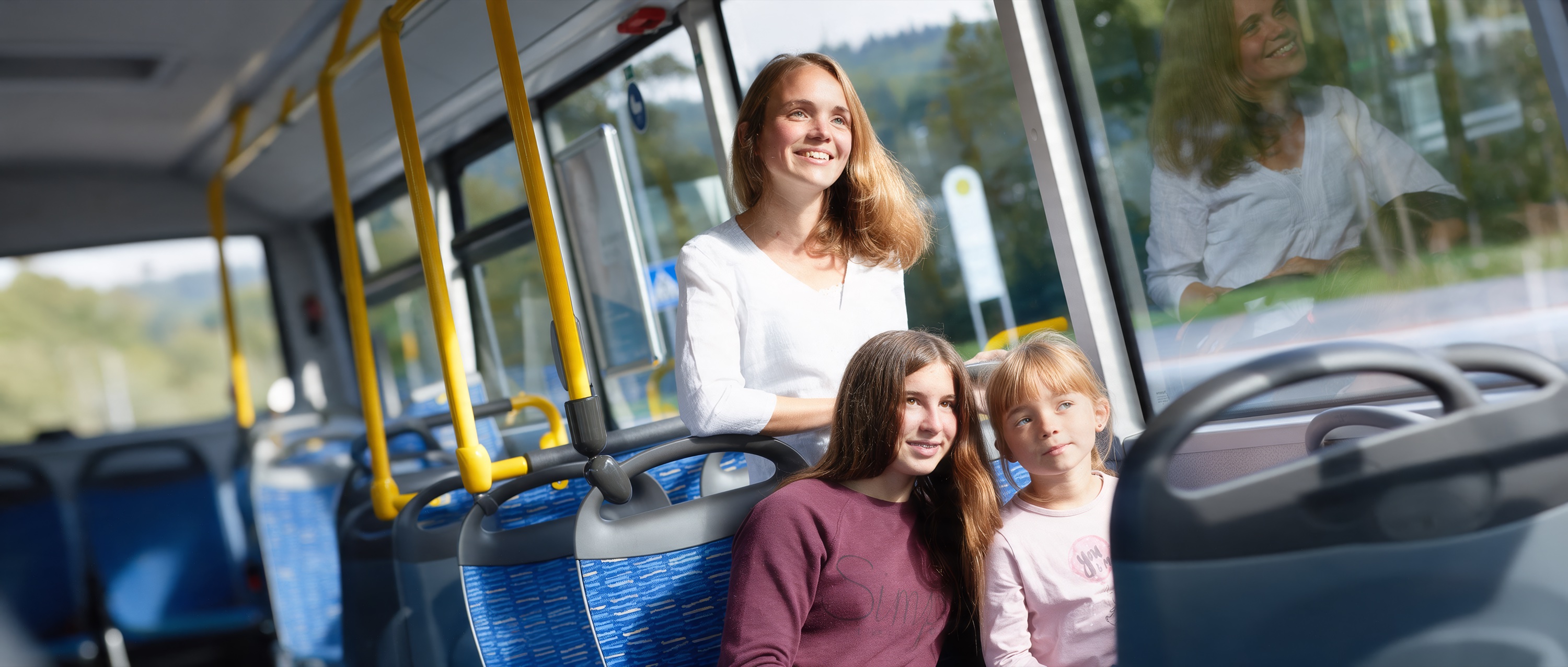 Mutter mit zwei Töchtern im Bus, die Mädchen sitzen und schauen lächelnd aus dem Fenster