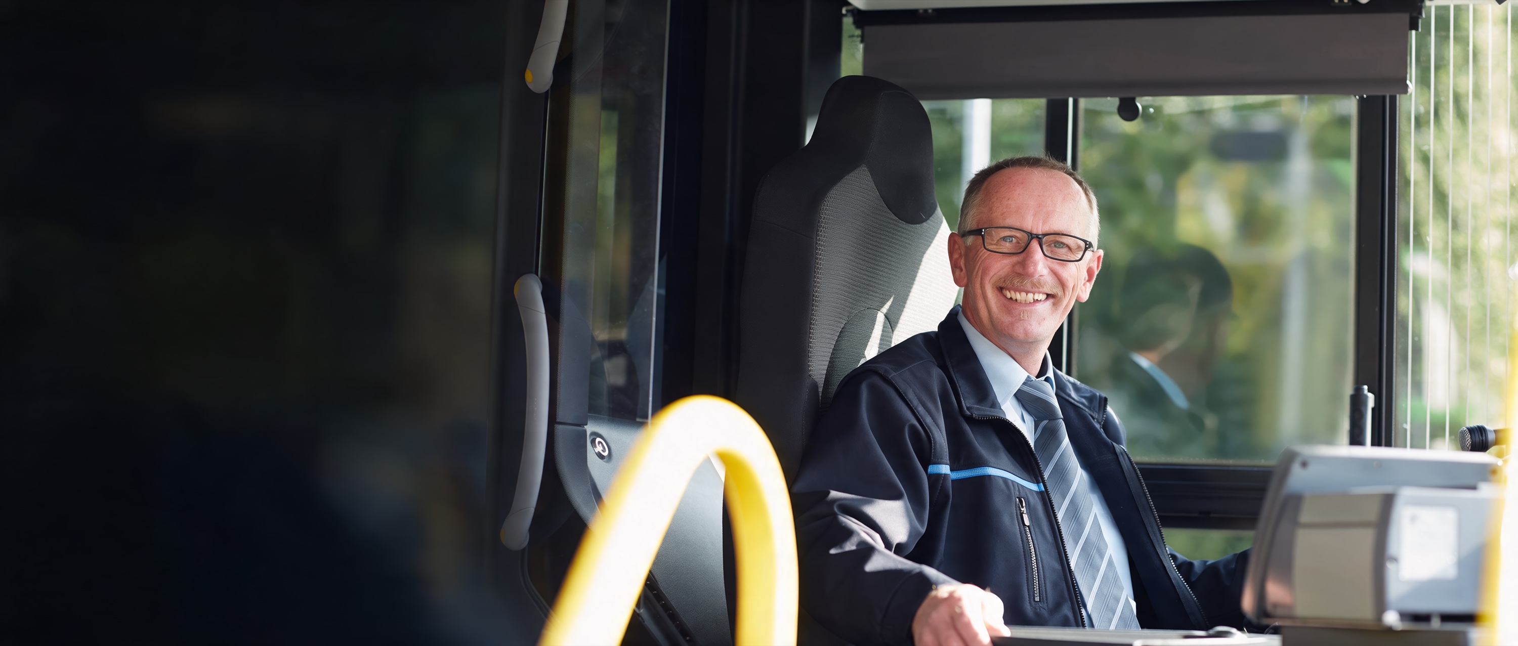 Lächelnder Busfahrer in Dienstkleidung sitzt am Steuer seines Busses