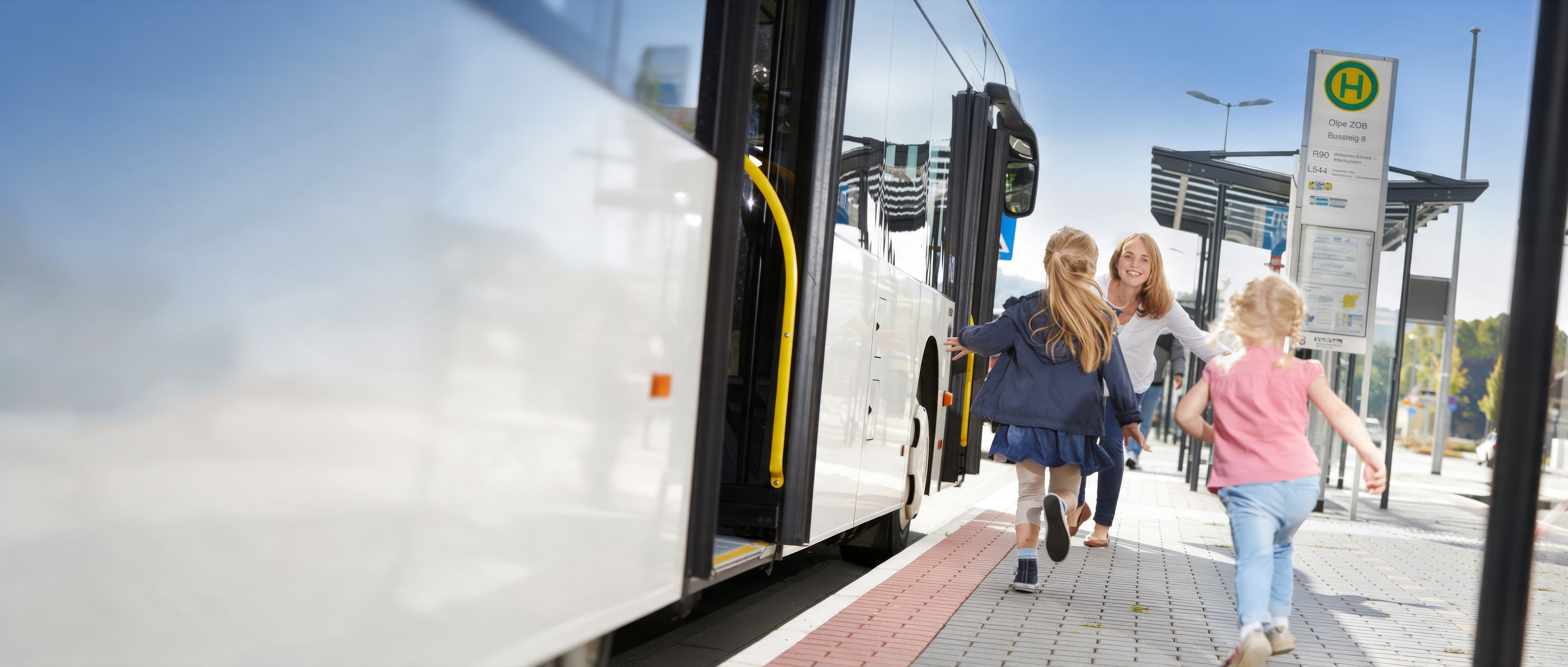 Mutter und zwei Mädchen laufen an der Haltestelle Olpe ZOB zum wartenden Bus